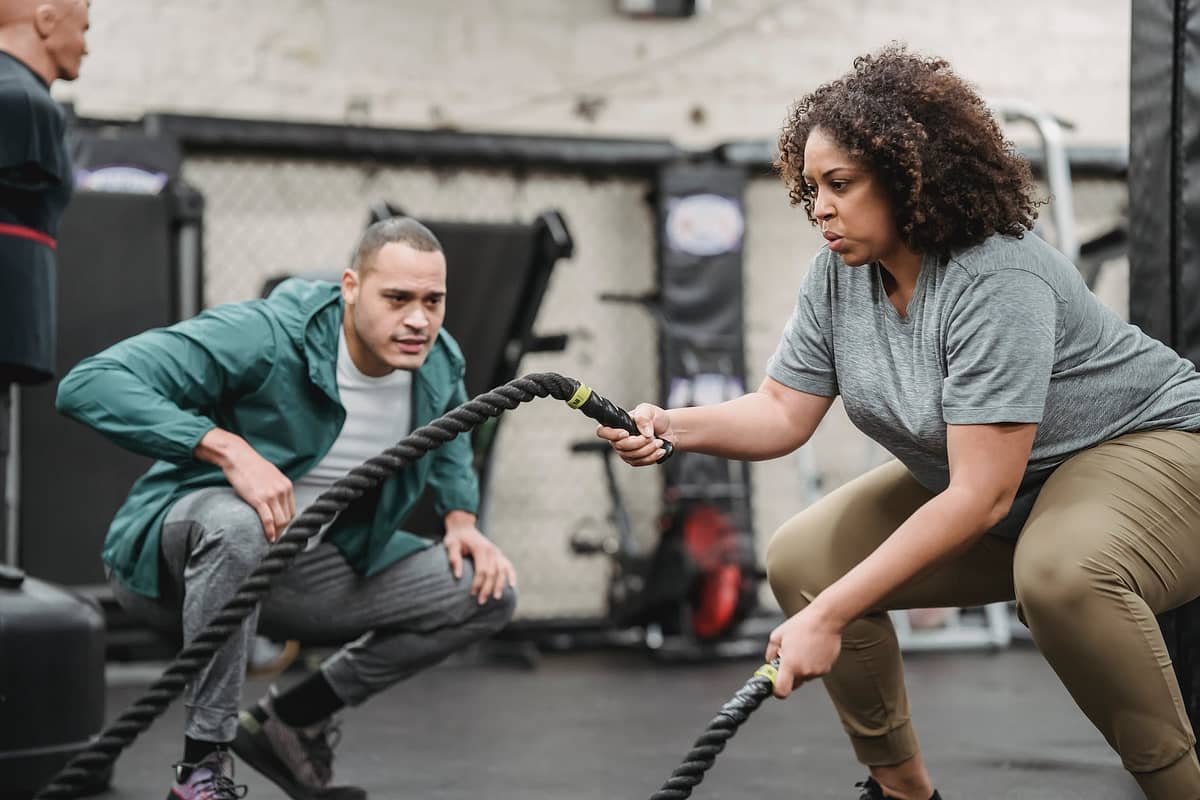 determined black plump woman exercising with battle ropes in gym