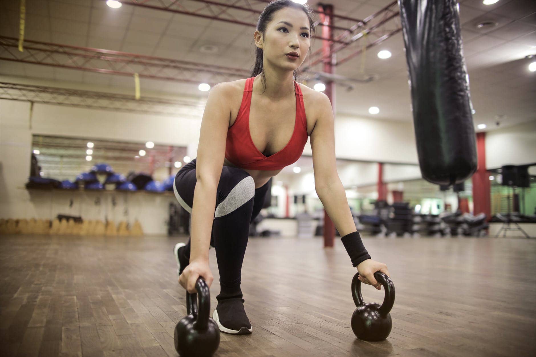 strong determined ethnic woman stretching body using kettlebells