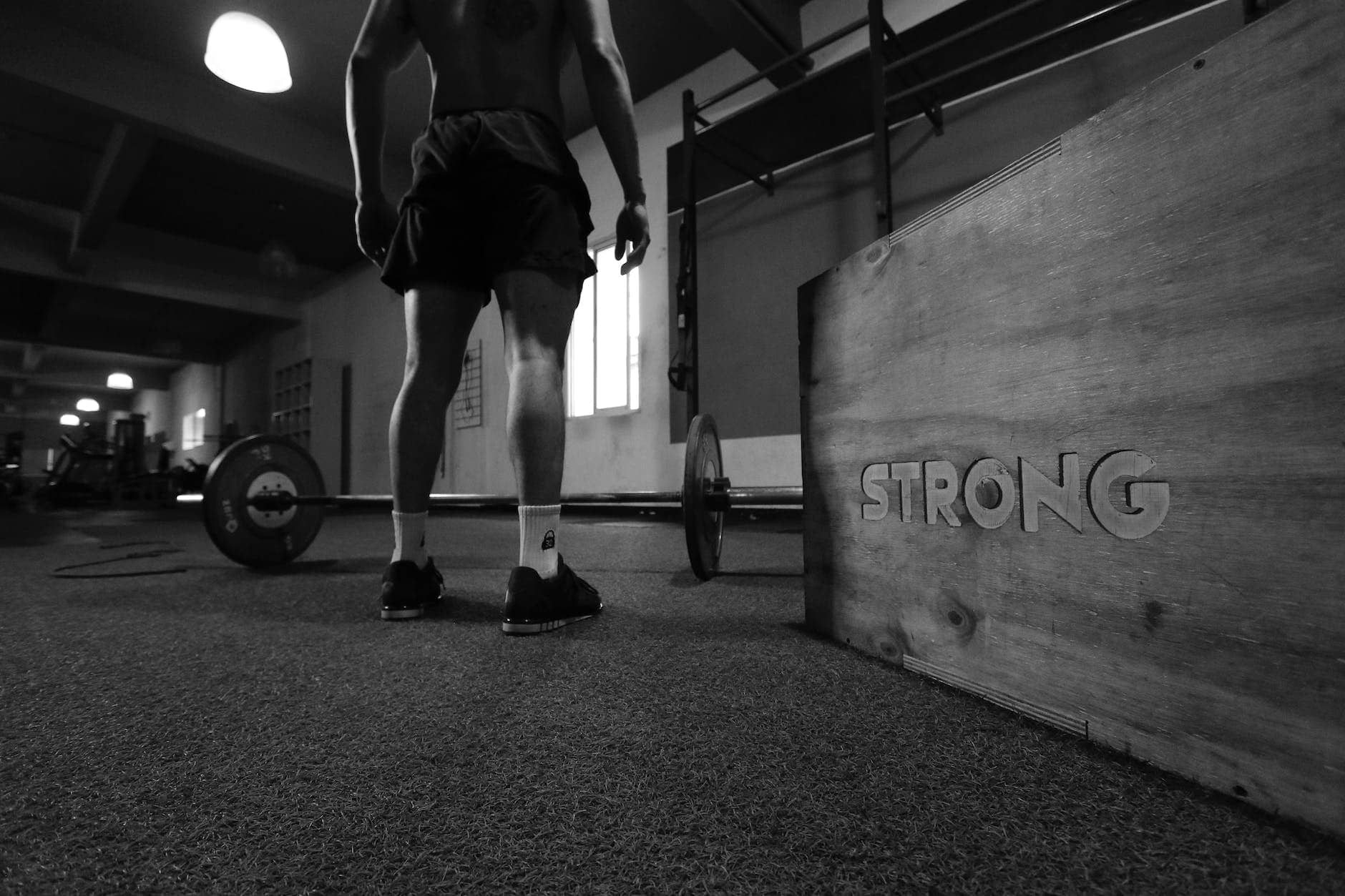 grayscale photo of man standing beside barbell