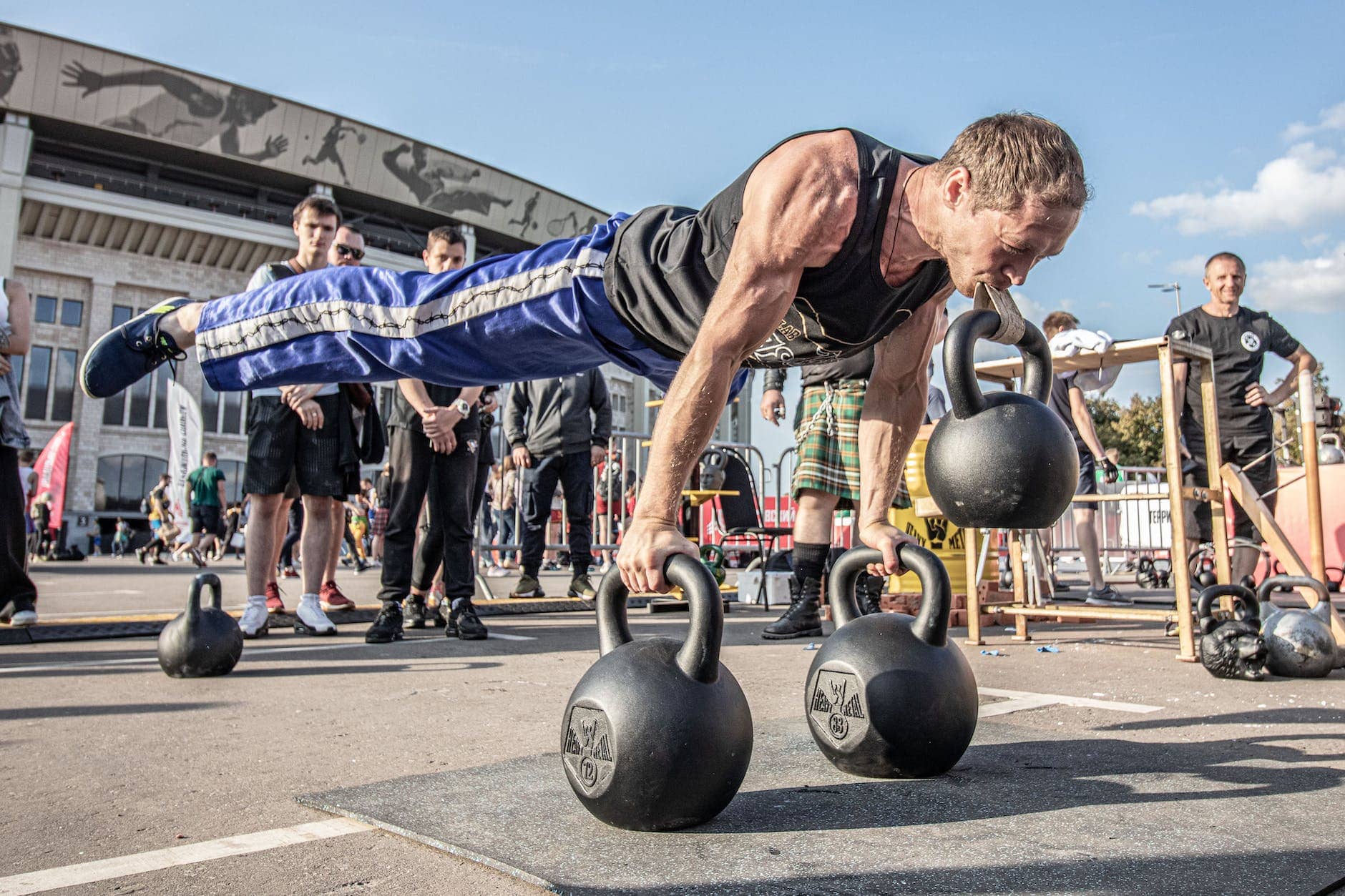 man in black tank top doing push ups with kettlebell on mouth